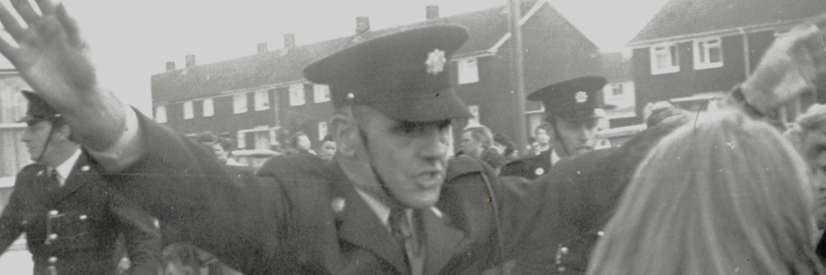 Old grainy black and white photo of a police officer holding up his arms, blocking peoples way