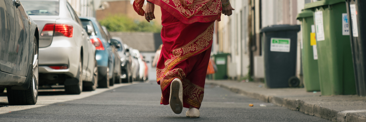 A lady in a red and gold sari, walking down a residential street.