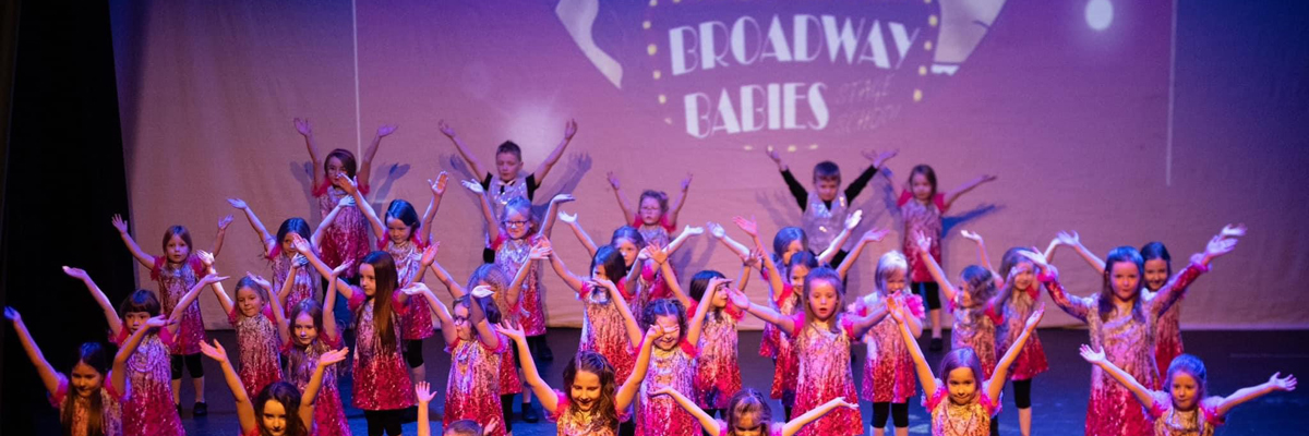 Young children with their arms raised, on a stage wearing sparkly red, gold and silver dresses and waist coats