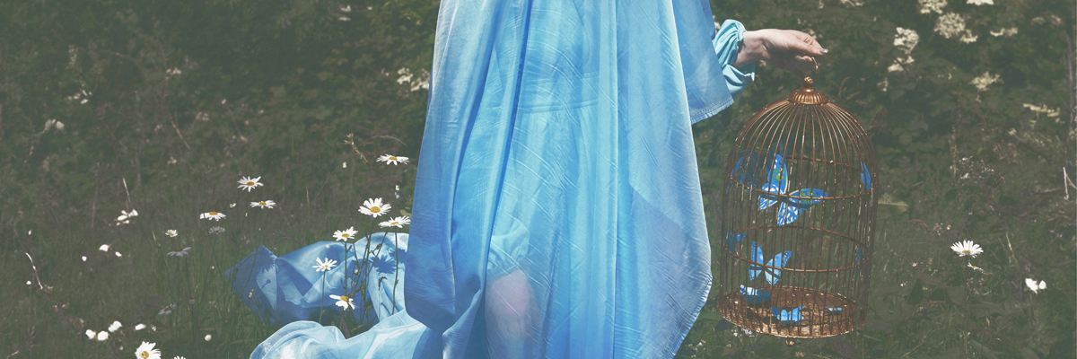 A lady draped in a bright blue, sheer fabric, carrying a brown bird cage with blue butterflies inside.