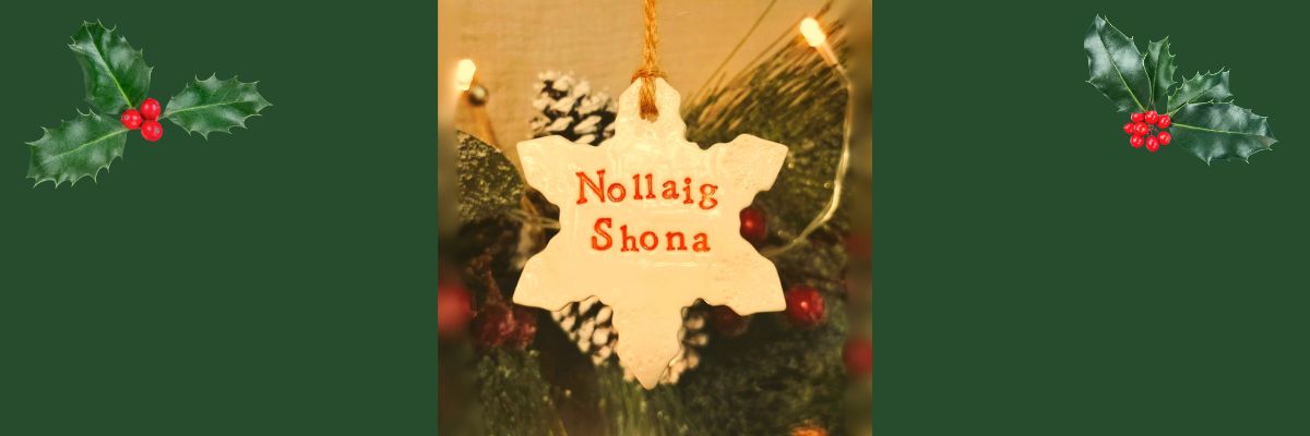 A ceramic Christmas ornament that says Nollaig Shona in front of a blurred Christmas Tree