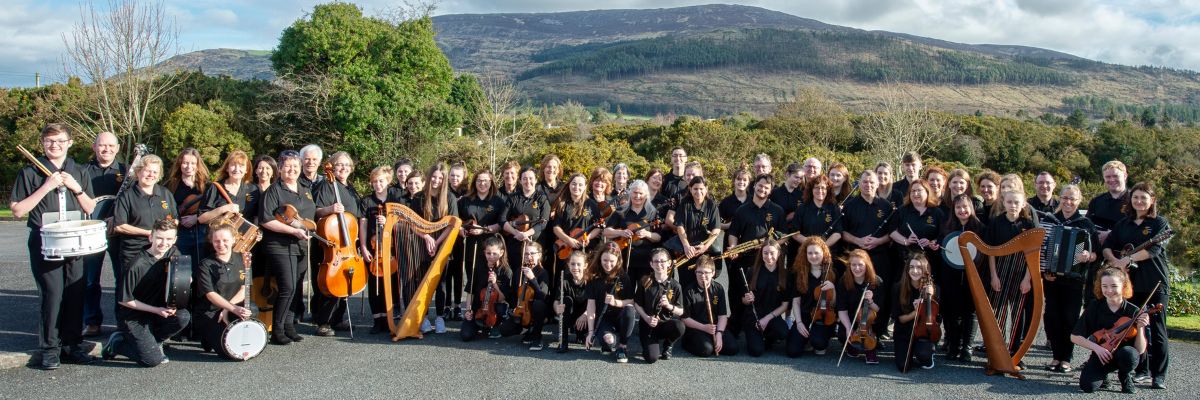 Oriel Traditional Orchestra members dressed in black stand against a backdrop of the Cooley Mountains